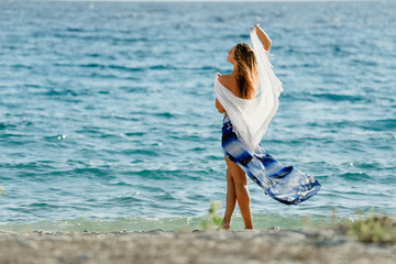 Fototapeta na wymiar Back view of feminine woman with a shawl by the sea.