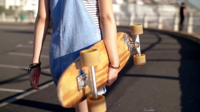 Teenage girl walking holding long board hipstermillennial woman with longboard