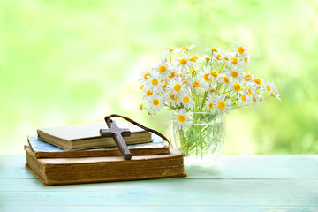 wooden cross, old religion books and chamomile flowers on wooden table. Christian cross and daisy...