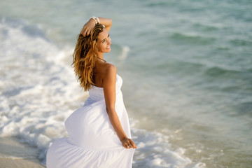 Obraz premium Beautiful woman in white dress at the shore during summer day.