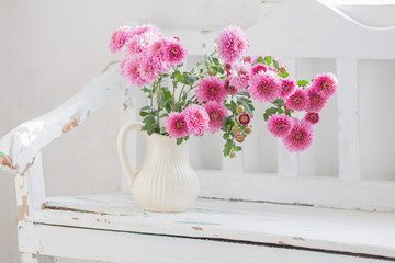 pink chrysanthemums in jug on old  white wooden bench