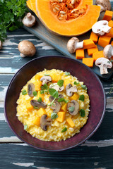 risotto con zucca gialla e funghi su tavolo di cucina rustico verde