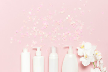Obraz na płótnie Canvas Cosmetics SPA branding mock-up Natural organic beauty product. Flat lay White cosmetic bottle containers festive confetti White Phalaenopsis orchid flowers on pink background top view
