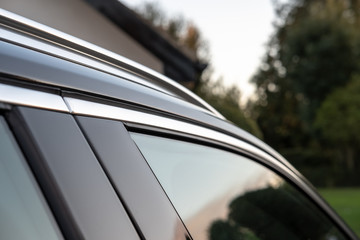 Detailed, shallow focus view of a Swedish-built SUV cars side door window and part of the metallic roof rack. Shown at a private residence.