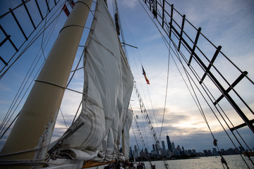 Gehisstes Segel auf Segelschiff in Abenddämmerung mit Skyline