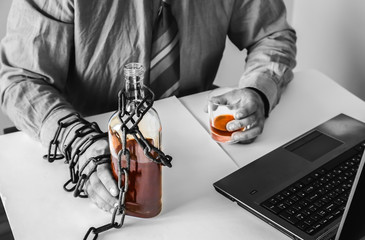 Man's hands in old rusty chains near the bottle. Addicted to alcohol. In the trap of office work....