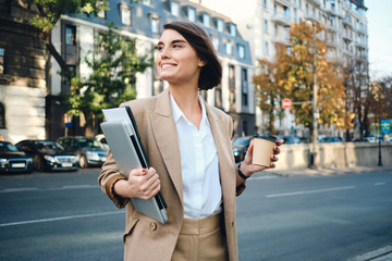 Fototapeta premium Young beautiful happy businesswoman with laptop and coffee to go on street
