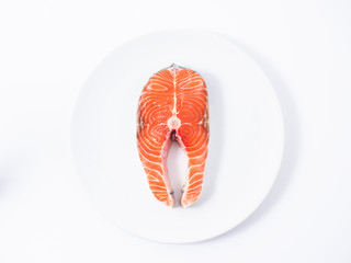 Raw salmon fillet on a white plate over white background. Top view