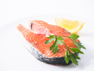 Raw salmon fillet on white studio background decorated with a lemon wedge and some parsley. Side view