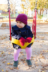 Vertical portrait of adorable toddler girl in playground yellow bucket swing during a beautiful late fall afternoon