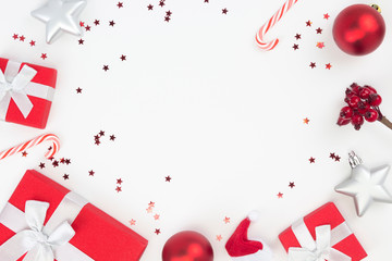 Frame from red Christmas gifts, balls, star confetti, candy canes on white background. Congratulation, Happy New Year concept. Top view, flat lay, copy space