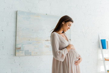 beautiful happy pregnant woman touching her belly at home