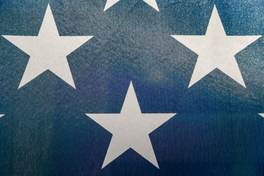 Close-up. attract view of white stars seen on a fabric United States national flag. Light can be seen illuminating from the rear of the flag.