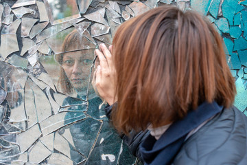woman looks in a broken mirror and shows her hand on a mirror. The concept of human emotions.