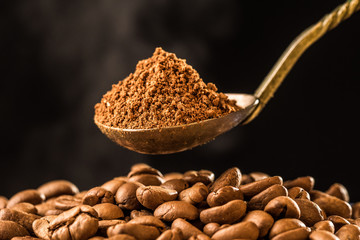 Roasting coffee beans into an old silver antique spoon on dark background. Smoke, steam of roasting coffee. morning fresh coffee aroma.