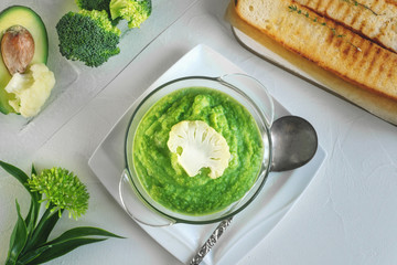 a bowl with vegetables puree on a white background. large white bowl with vegetable green cream soup of broccoli, zucchini, green peas on white background, top view