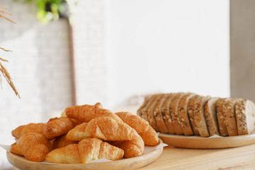 Slices bread and delicious croissant on wooden table background. Breakfast concept.