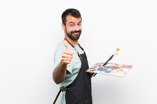 Young artist man holding a palette over isolated background with thumbs up because something good has happened