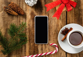 Mock up blank empty screen of smartphone on the wooden background with colorful holiday's decoration, tea and gifts. Copyspace, negative space for your advertising. 31 of December, New Year concept.