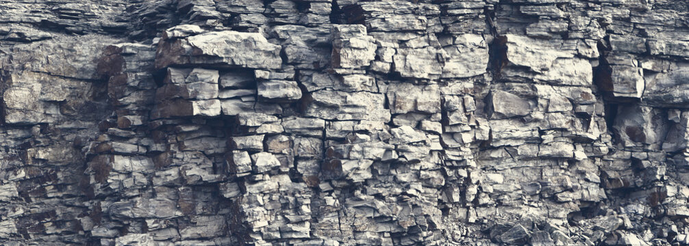 Dangerous vertical wall with protruding crumbling layered wild stone blocks. Rock cliff face background. Toned. Abstract texture for stone mining industry. Copy space for custom text
