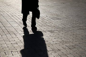 Black silhouette and shadow of man in raincoat with briefcase walking on the street. Concept of...