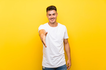 Young handsome man over isolated yellow background shaking hands for closing a good deal
