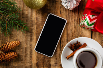 Mock up blank empty screen of smartphone on the wooden background with colorful holiday's decoration, tea and gifts. Copyspace, negative space for your advertising. 31 of December, New Year concept.