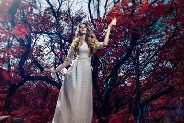 Beautiful girl in white long dress in the fairytale autumn forest with red foliage like an...