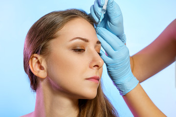 Portrait of beautiful young girl in beauty parlor. Cosmetology injections, hands in medicine gloves holds syringe