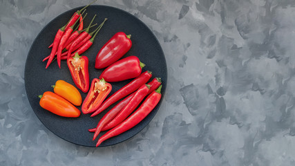 Colorful mix of the freshest and hottest chili peppers and Bulgarian colored pepper on a black plate.
