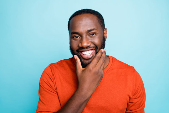 Closeup photo of attractive dark skin guy toothy beaming smiling touch cheekbones check beard growth temp wear orange pullover isolated blue color background