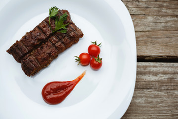 Food in the restaurant. Grilled pork with cherry tomatoes. White plate on a wooden bottom.