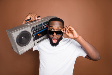 Photo of astonished casual man holding retro audio recorder wearing white t-shirt and eyewear sunglass isolated over pastel color brown background listening to music © deagreez