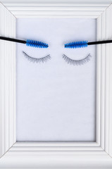Beautiful eyelashes and eyebrows concept: white photo frame decorated with eyelash extensions and tools and gift on white background.