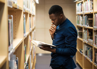Young black man choosing book in public library