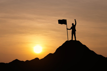 Silhouette of businessman holding a flag on top mountain, sky and sun light background. Business success and goal concept.