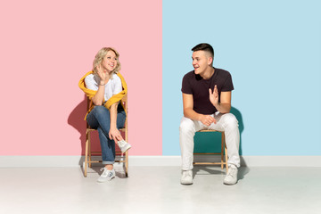 Obraz premium Young emotional man and woman in bright casual clothes posing on pink and blue background. Concept of human emotions, facial expession, relations, ad. Beautiful caucasian couple greeting, talking.