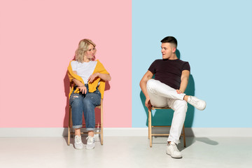 Obraz premium Young emotional man and woman in bright casual clothes posing on pink and blue background. Concept of human emotions, facial expession, relations, ad. Beautiful caucasian couple greeting, talking.