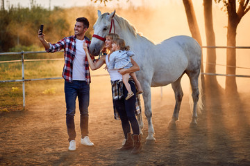 Smiling family with girl in a horse farm make selfie
