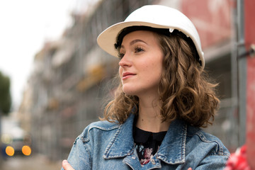 Profile portrait of a pretty and young female factory worker wearing a white protective helmet