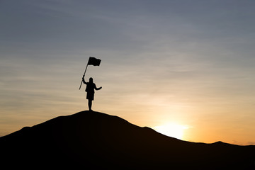 Silhouette of businesswoman holding a flag on top mountain, sky and sun light background. Business success and goal concept.