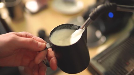 Barista steaming milk in frothing pitcher in slow motion