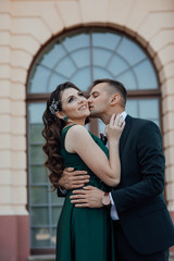 Stylish couple pose on building background. Amazing photo of a lovely girl kissed by her boyfriend on the forehead while traveling.