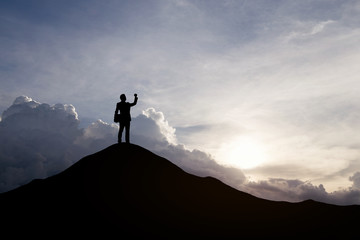 Silhouette of businessman raising his hand to celebrate success on top mountain, sky and sun light background.