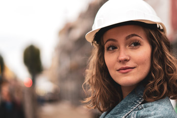 Close-up portrait of a pretty and young female factory worker wearing a white protective helmet