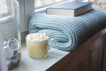 Heiße, weiße Trinkschokolade mit Sahne und Marshmellows Fensterbank mit gemütlicher Wolldecke...