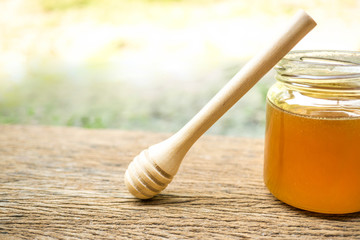 Honey scoop and jar of honey on old wood.