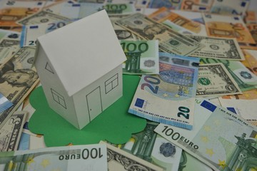 Paper model of a house on a background of banknotes of dollars and euros, background