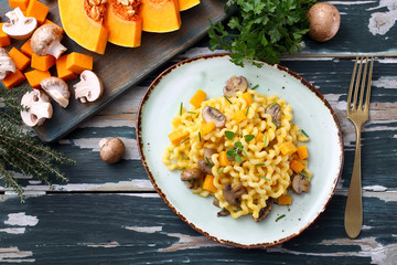 pasta maccheroni con zucca gialla e funghi su tavolo di cucina verde rustico