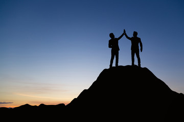 Silhouette of people are celebrating success at the top of the mountain, sky and sun light background. Team business concept.